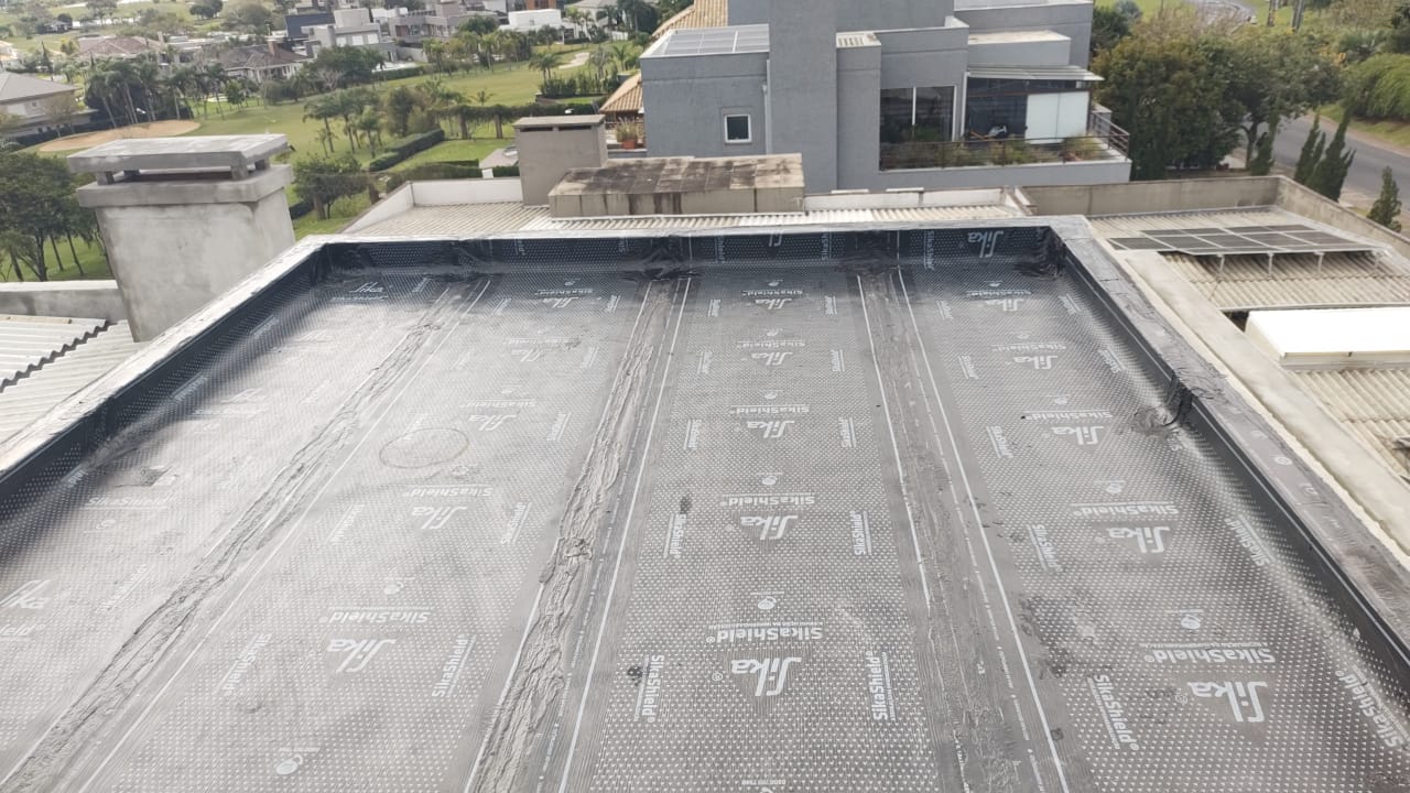 Serviço de impermeabilização de laje com manta asfáltica em andamento.